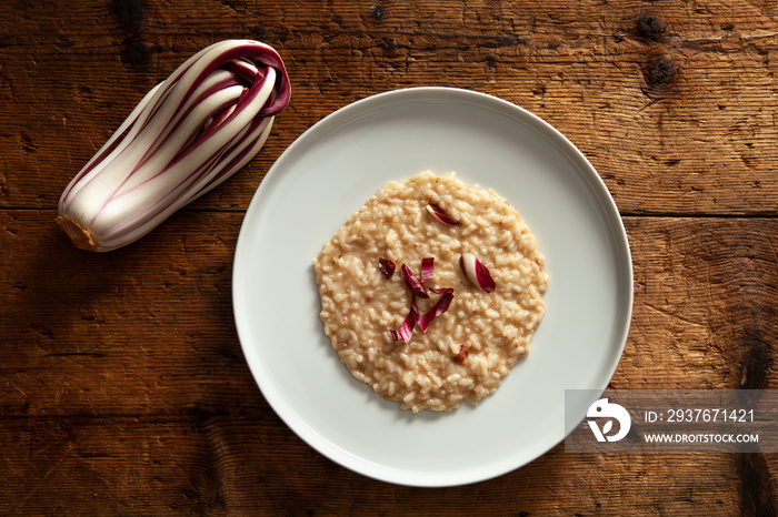 risotto with Treviso red radicchio and sausage. plate of risotto on top of wooden table. view from a