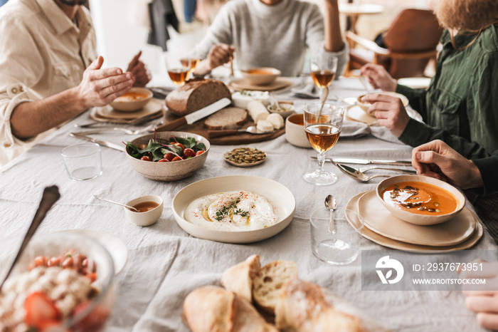 Close up group of young people sitting at the table full of delicious food and glasses of wine havin