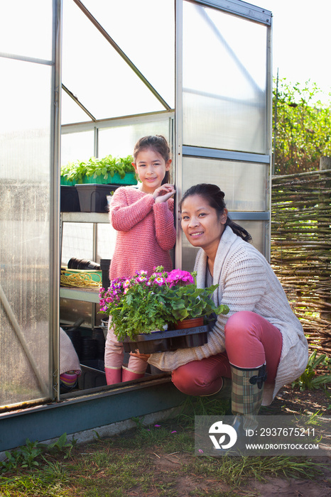 Mother holding plants with daughter in greenhouse