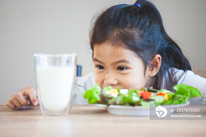 Cute asian child girl eating healthy vegetables and milk for her meal