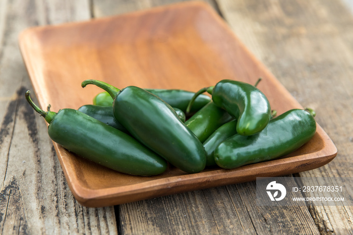 a pile of large spicy green organic Jalapeños on a wood tray