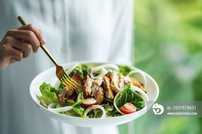 Closeup image of a woman holding and eating chicken salad