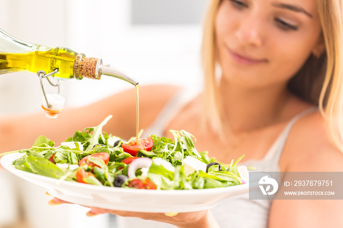 Young happy blonde girl eating healthy salad from arugula spinach tomatoes olives onion and pouring 