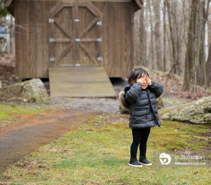 Little girl covering her eyes and standing in forest