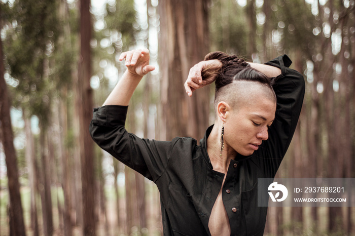 Hipster woman holding hair while practicing contemporary dance in woodland