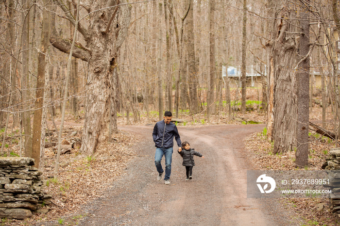 Father and daughter holding hands while walking on road amidst bare trees in forest