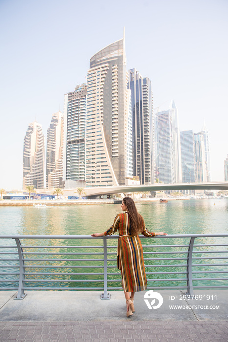 Rear view of happy beautiful tourist woman in fashionable summer white dress enjoying in Dubai marin