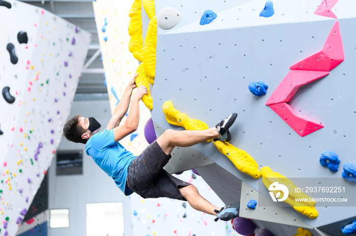 View of a man wearing a COVID-19 pandemic mask climbs a bouldering wall in a climbing gym following 