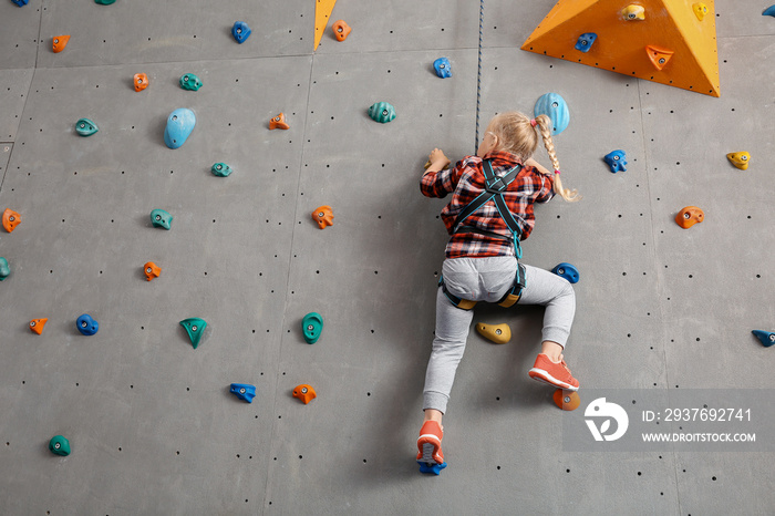 Little girl climbing wall in gym