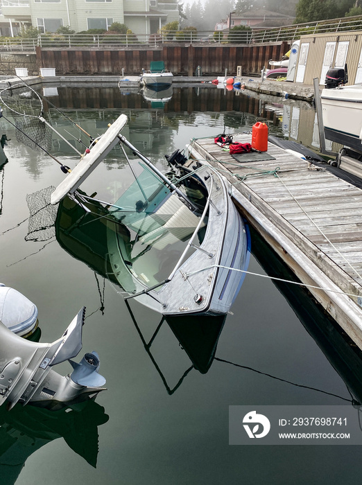 An aluminum fishing boat is sinking at its slip on the dock, and is filling up with water quickly a