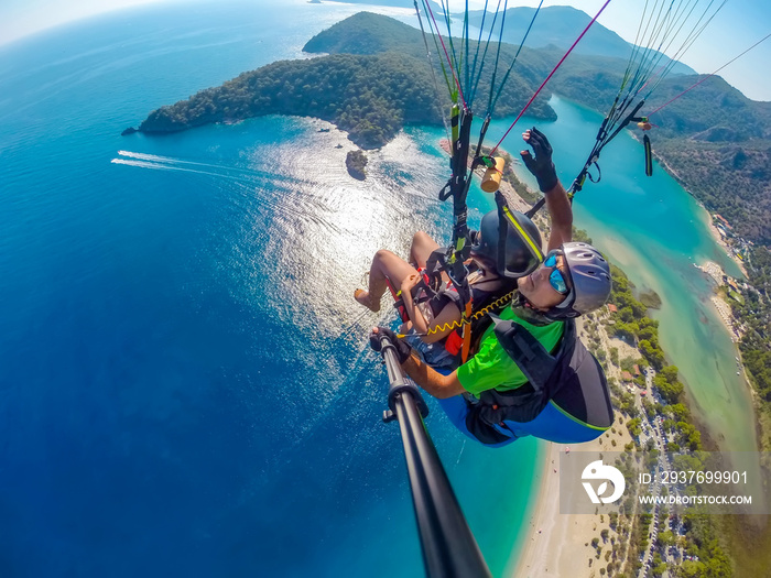 Paraglider tandem flying over the sea with blue water and mountains in bright sunny day. Aerial view