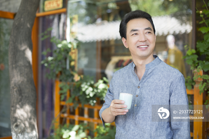 男性店主拿着茶杯站在店外