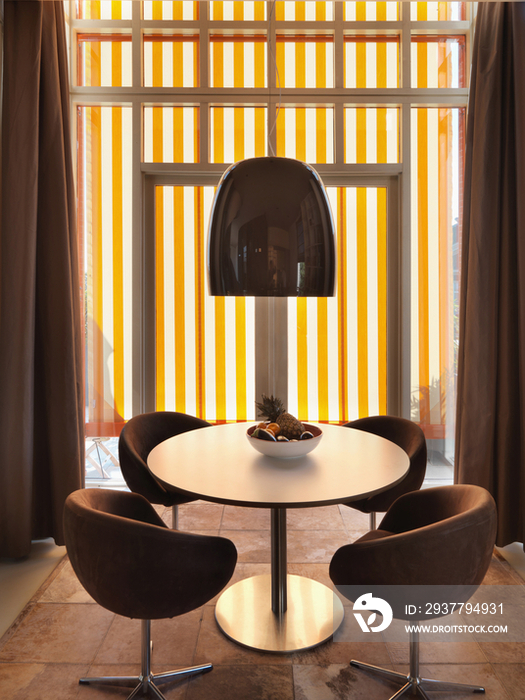 Four elegant chairs at round table against window and striped background