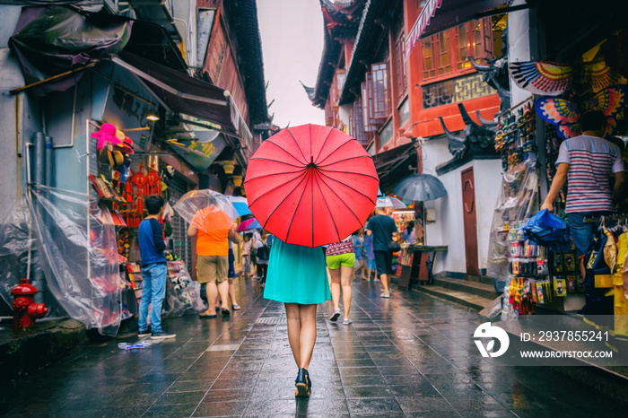 走在唐人街购物街上的妇女。雨天女孩游客在红色东方伞下