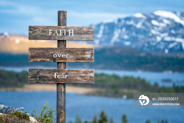 faith over fear text quote on wooden signpost outdoors in nature during blue hour.